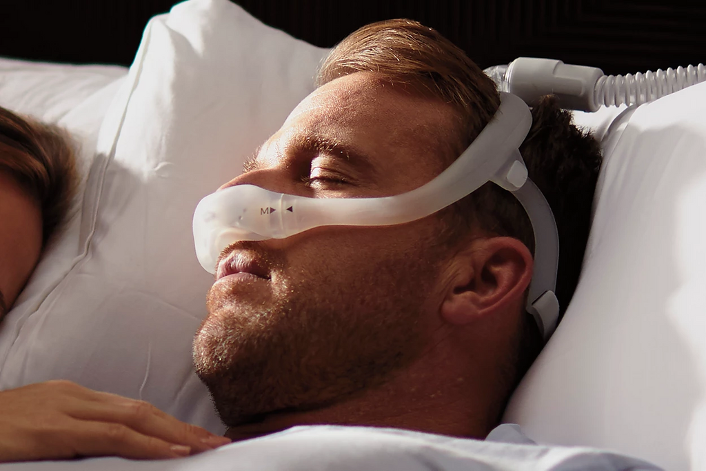 Close-up of a man sleeping in bed, wearing the Philips Respironics DreamWear under-the-nose nasal mask.