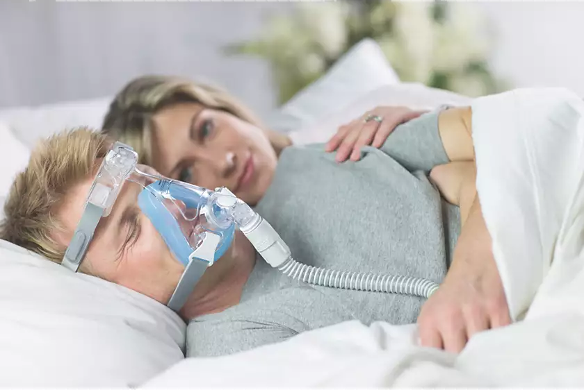 A person using a Philips Respironics Amara Gel Full Face CPAP mask with a partner looking on in bed.