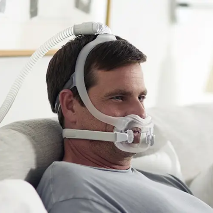 A man wearing a Philips Respironics DreamWear Full Face CPAP mask connected to a CPAP machine.