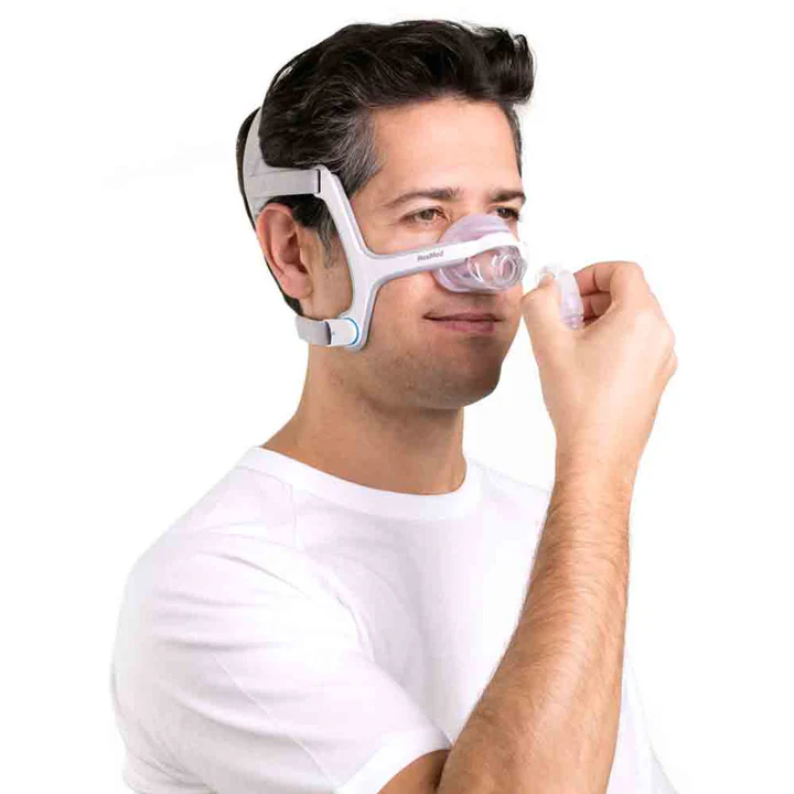A man removing the QuickRelease Elbow from the ResMed AirFit N20 Nasal Mask while wearing it.